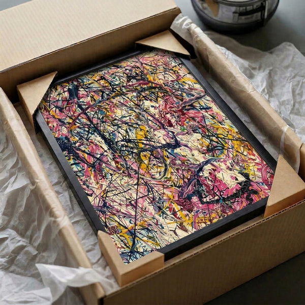 Vibrant abstract splatter art combining pink, yellow, and blue tones with dynamic black brushwork on a cream-colored canvas, framed as modern wall decor.