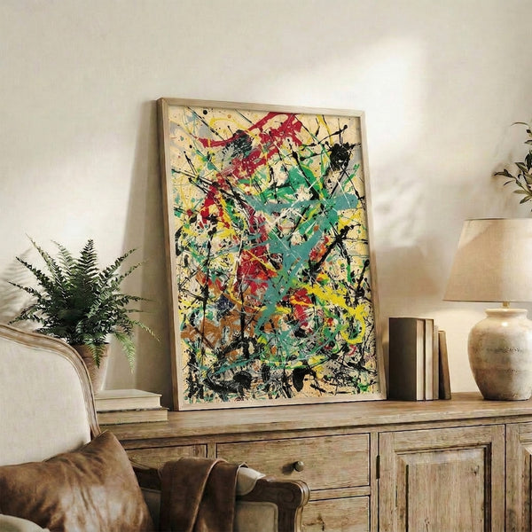 Framed modern abstract print with explosive splatter composition in bold crimson, teal green, and bright yellow against cream surface.