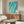 Peaceful coastal wall art depicting a solitary surfer on rolling waves in soothing teal and turquoise tones with minimalist watercolor styling and coral accents.