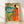 Watercolor folk art portrait of a Maasai woman in traditional beaded dress standing in a savanna landscape with trees and golden fields, rendered in terracotta, forest green, coral, and turquoise tones.