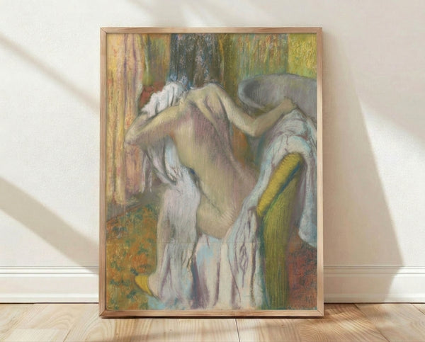 Framed Degas poster depicting a woman in soft pastels drying herself after bathing, rendered in impressionist style with warm ochre and blue tones.
