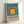 Minimalist poster displaying layered squares in periwinkle, teal, rust, and gold creating optical depth; contemplative geometric artwork on wall.
