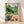 Vintage Art Nouveau woodblock print depicting a serene mountain landscape with a teahouse window framing a teapot and teacup, rendered in forest green, cornflower blue, terracotta, and cream tones.