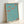 Framed art print displaying Art Nouveau clover design with flowing lines in muted turquoise and terracotta hues on cream background.