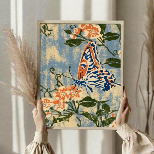 Framed botanical wall art depicting a graceful monarch butterfly with ornate patterned wings in warm coral tones, complemented by naturalistic flowers and leafy sprays in cream, soft blue, and dark green.