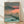 Japanese woodblock print depicting a serene autumn lake at sunset, with layered mountains in charcoal grey, golden trees reflected in deep teal waters, and a coral pink sky creating a contemplative mood.
