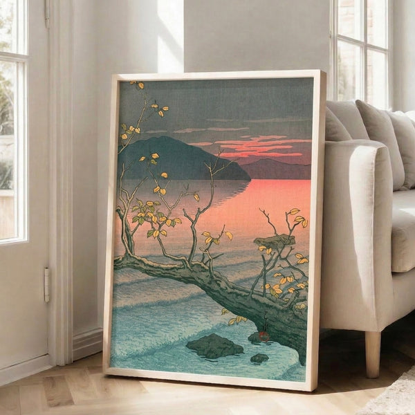 Framed wall art in traditional woodblock style showing a contemplative autumn lake scene with charcoal mountains, golden trees, and warm peachy-pink sunset light over still teal waters.