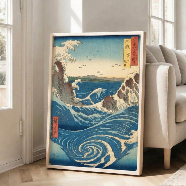 Traditional Japanese woodblock print framed on wall showing majestic Naruto whirlpool with dramatic blue and turquoise waves, cream highlights, brown rocks, and birds in flight against pale yellow sky.