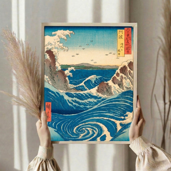Framed Japanese woodblock print featuring serene yet dramatic whirlpool surrounded by rocky outcrops in cream and brown, set against prussian blue and turquoise ocean with pale yellow atmospheric tones.