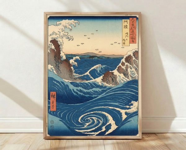 Framed Japanese woodblock print depicting a dramatic whirlpool with swirling deep blue waters, rocky cliffs, and birds flying across a pale sky in rust and cream tones.