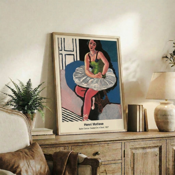Framed modern art poster showing a seated ballet dancer in characteristic line-art style, palette of ochre, tan, black, and white conveying quiet introspection.
