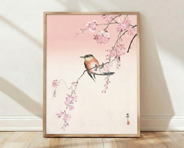 Serene Japanese woodblock-style art print depicting a bird perched on delicate cherry blossom branches in soft pink and cream tones, framed on a wall.