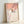 Framed poster showing a graceful bird on blooming cherry branches in muted coral orange and cream hues, inspired by traditional Japanese woodblock aesthetics.