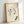 Wall-mounted poster of Japanese woodblock artwork featuring graceful circling birds and an insect among botanical elements, rendered in soft cream and black with touches of pale green.
