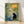 Serene minimalist poster featuring a black cat beside a traditional bamboo lantern amid delicate flowers and foliage in cream, sage green, and soft yellow tones, evoking a tranquil Japandi garden.