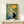Framed Japandi art print with a contemplative black cat gazing at an illuminated lantern nestled in bamboo and flowering plants rendered in soft, muted earth tones.