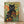Black cat with golden eyes sits among vibrant wildflowers in art nouveau style, surrounded by gerberas and daisies in warm oranges and yellows against forest green foliage.