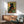 Enchanted garden wall art in art nouveau style depicting a contemplative black cat surrounded by vibrant gerberas, daisies, and foliage in golden yellow and burnt orange hues.