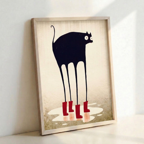 Modern wall art print showing a playful black cat adorned with red rain boots, poised over a puddle in minimalist line drawing style on a cream canvas.
