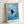 Whimsical framed poster showing a black cat observing water ripples and fish with delicate line work in a serene blue and white composition.