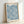 Framed Art Nouveau wall art displaying stylized marigold flowers in teal and navy with intricate leaf patterns on cream, elegant botanical design.