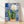 Watercolor painting of a blooming cactus in a terracotta pot adorned with cobalt blue and golden yellow Talavera tile patterns, rendered in soft washes against cream and white, creating a cheerful boho botanical aesthetic.