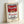 Framed modern pop art print of a Campbell's soup can label, combining ironic commentary on mass production with vibrant red and metallic gold tones.