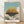 Whimsical framed poster of a floating castle nestled among soft clouds, rendered in dreamy teal, cream, and warm tan tones with charcoal accents in the Studio Ghibli aesthetic.