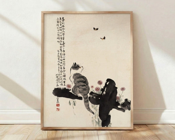 Framed Japanese woodblock-style poster featuring a tabby cat gazing upward at butterflies and flowering branches in cream, black, and mauve tones.