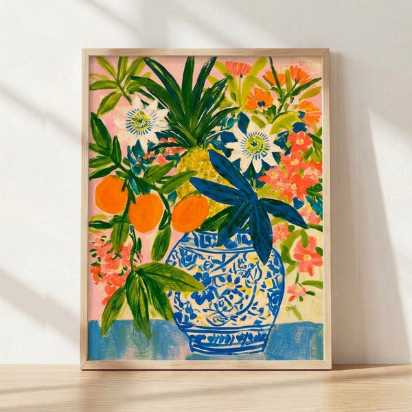 Watercolor botanical print featuring a blue and white vase overflowing with pink passionflowers, orange citrus blooms, and chartreuse leaves on a cream background, framed on a wall.