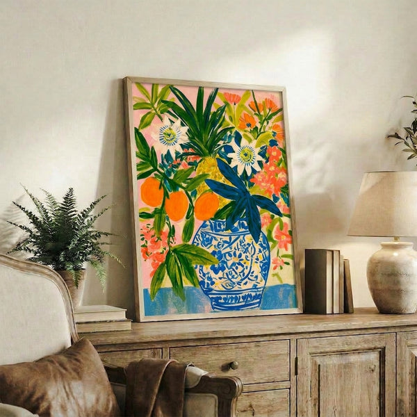 Framed modern watercolor artwork of vibrant citrus and passionflower bouquet in shades of pink and orange sprouting from a deep blue vase with botanical foliage.