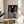 Framed kinetic wall art depicting surreal stone figures overlooking a starlit abstract landscape with geometric planets, blending monochromatic and coral tones in an imaginative composition.