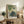 Contemplative Impressionist garden painting with a woman surrounded by flowers and foliage in delicate tones of soft green, warm ochre, and pale blue creating a peaceful mood.