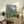 Framed poster of an intimate outdoor conversation beneath gnarled olive trees, painted in muted greens and ochres with an impressionistic, relaxed composition.