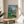 Abstract landscape print portraying figures in dialogue beneath olive foliage, rendered in soft, naturalistic hues with a peaceful, introspective quality.