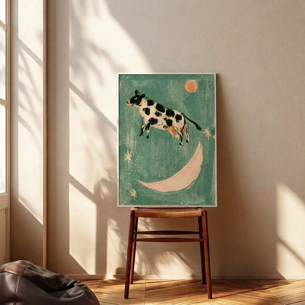 Cottagecore wall art depicting a graceful cow in mid-leap over a luminous moon surrounded by twinkling stars, done in soft vintage palette of sage green and cream with black accents.