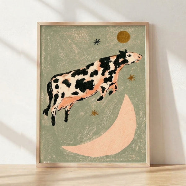 Whimsical folk art poster of a cow leaping over a crescent moon surrounded by stars, rendered in retro style with sage green, cream, black, terracotta, and golden yellow tones, framed on a wall.