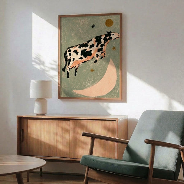Retro folk art framed poster depicting a whimsical cow mid-leap over a golden crescent moon with scattered stars, composed in muted sage, cream, and terracotta hues with a dreamlike quality.