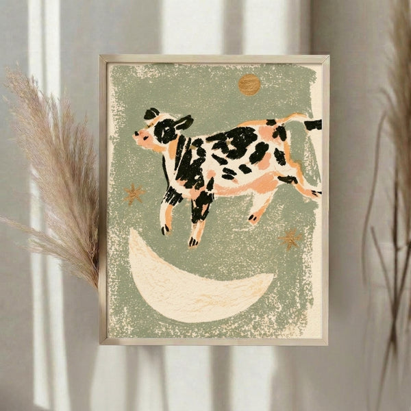 Framed nursery art print depicting a charming cow in mid-leap over a golden moon with stars scattered across a sage and cream palette, evoking vintage storybook nostalgia.