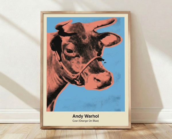 Bold pop art cow head print in vibrant orange and blue with bright yellow-green accents, framed on wall in contemporary style.