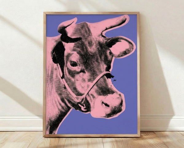 Pop art poster featuring a cow's head in vibrant pink against a bold purple background, displayed as a framed wall print in a modern interior.