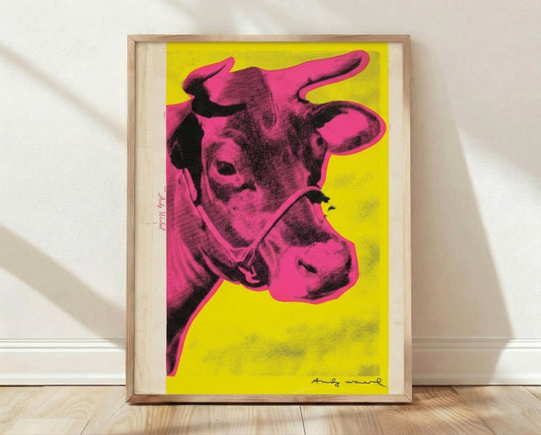 Pop art poster featuring a stylized cow head in bright pink against a vibrant yellow background, framed on a wall.