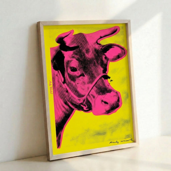 Contemporary wall art displaying a simplified cow portrait in hot pink tones contrasting with a golden yellow backdrop.