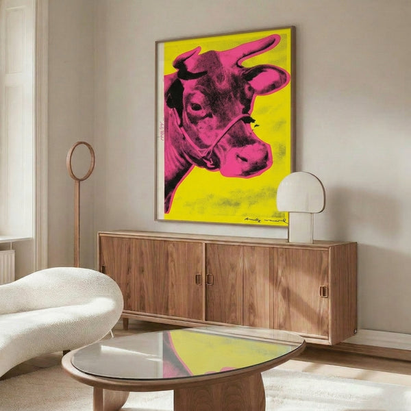 Modern art poster with a graphic pink cow illustration against a bright yellow background, displayed as framed wall décor.