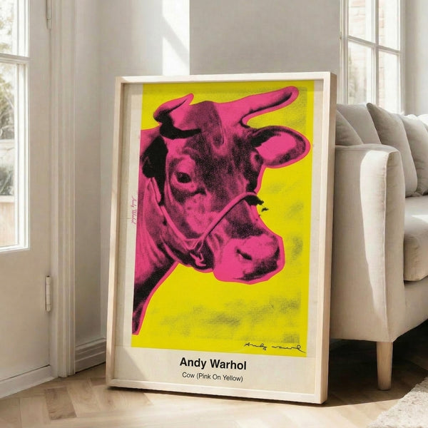 Vibrant pop art print of a cow's face in pink tones against bright yellow, featuring bold black graphic elements and irreverent kitsch aesthetic.