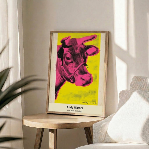 Modern pop art framed poster depicting a stylized cow portrait in pink and yellow with graphic black accents, gallery-style wall display.