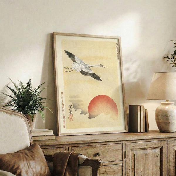Framed Japanese wall art depicting a poised crane in flight against a glowing red sun, combining serene aesthetics with Japandi design sensibility.