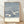 Serene Japanese woodblock-style poster featuring two cranes in falling snow amid winter forest, rendered in slate blue, cream white, and navy tones with red accent details.