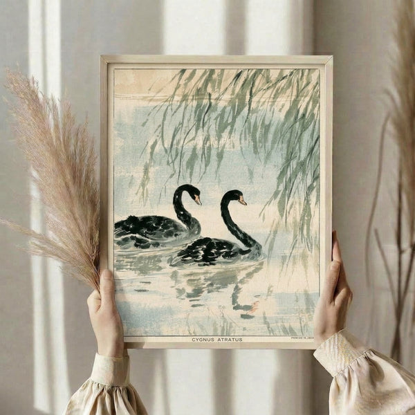 Minimalist black swan framed wall art inspired by Japanese woodblock prints, depicting the bird in a serene water landscape with willow branches and water lilies in soft sage and blue-cream tones.