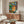 Minimalist modern art poster of a woman amid ornamental textiles and geometric forms, rendered in a rich palette of teal, burgundy, gold, and cream tones.